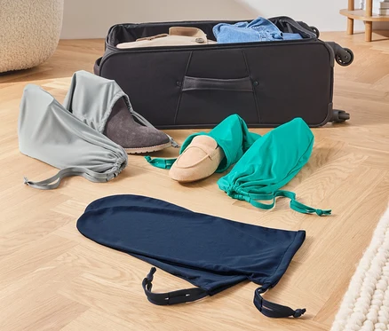 Sur le sol reposent une valise ouverte et trois 6 sacs à chaussures et à linge pour le voyage.