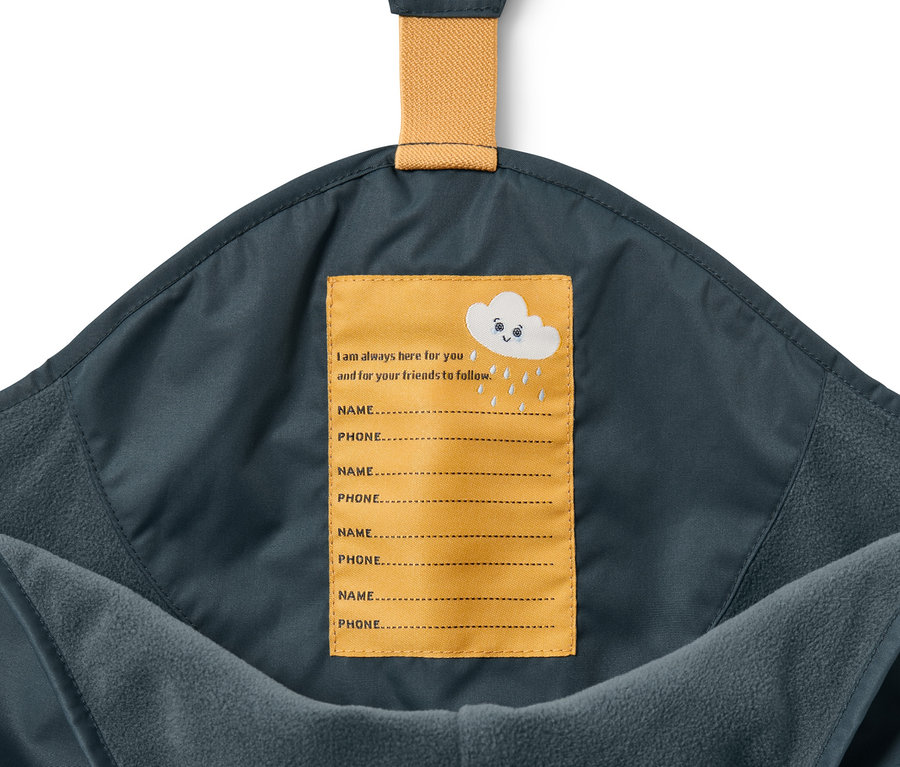 Détail d'un pantalon de pluie thermique pour enfant bleu ardoise avec une étiquette de nom jaune.