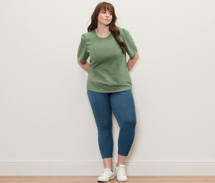 Femme posant dans une chemise verte avec des fronces et un jegging.