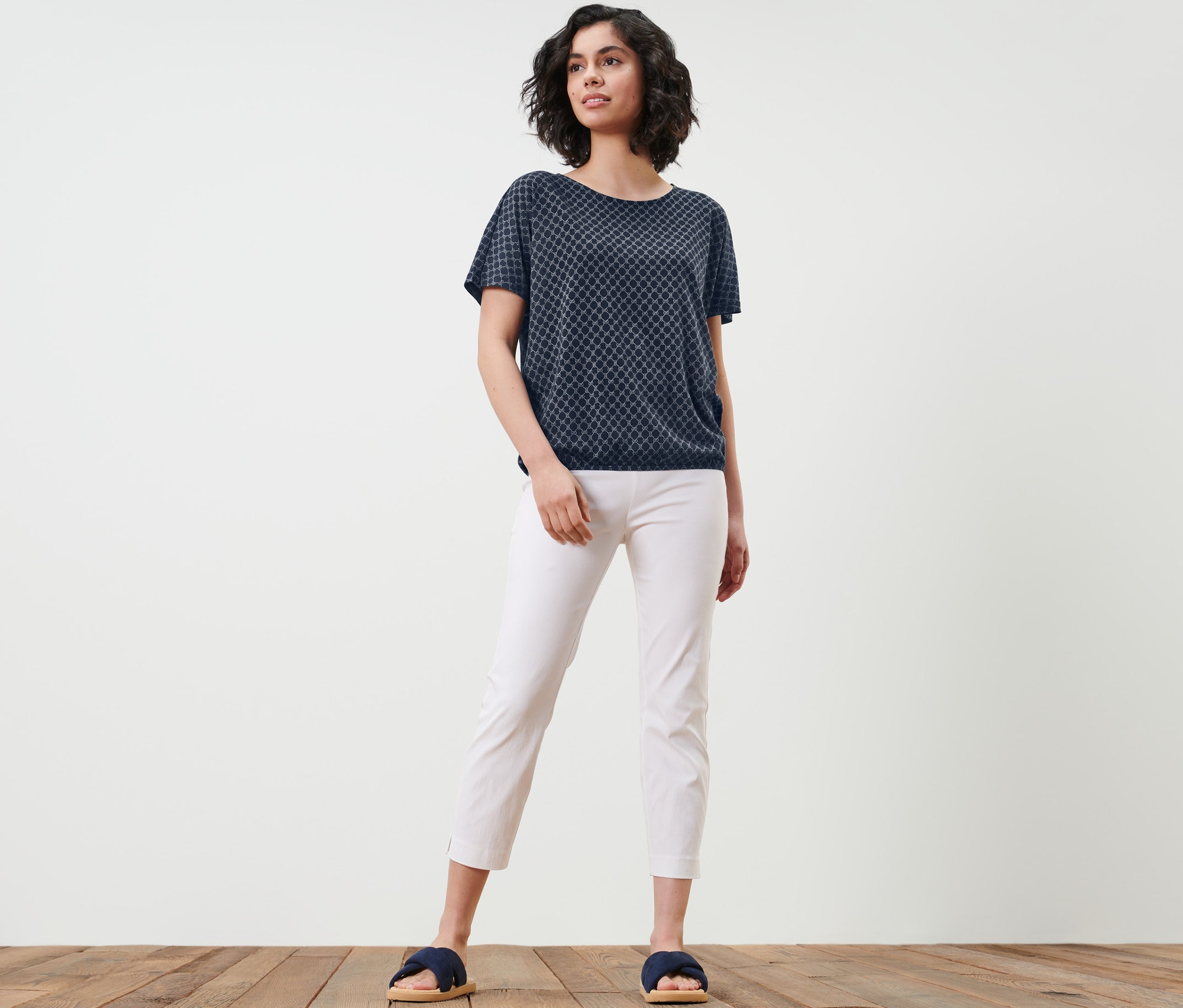 Femme posant dans une blouse imprimée, un pantalon blanc et des mules.