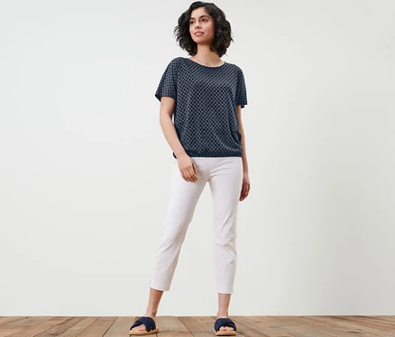 Femme posant dans une blouse imprimée, un pantalon blanc et des mules.
