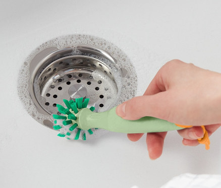 Une femme nettoie l'évier avec une brosse de nettoyage universelle.