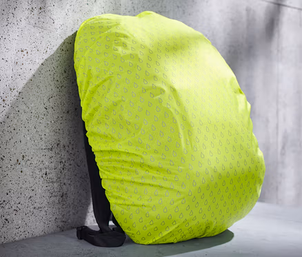 Housse de protection jaune pour sac à dos avec motif de gouttes sur un sac à dos appuyé contre un mur.