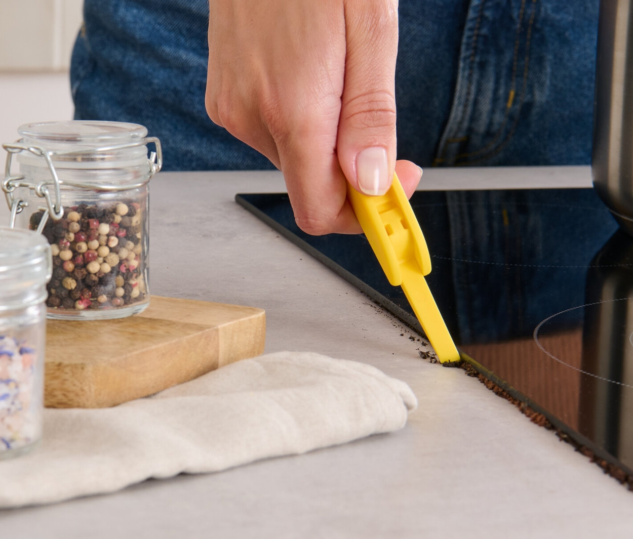Une femme nettoie le bord d'une plaque vitrocéramique avec une brosse de nettoyage 3 en 1.