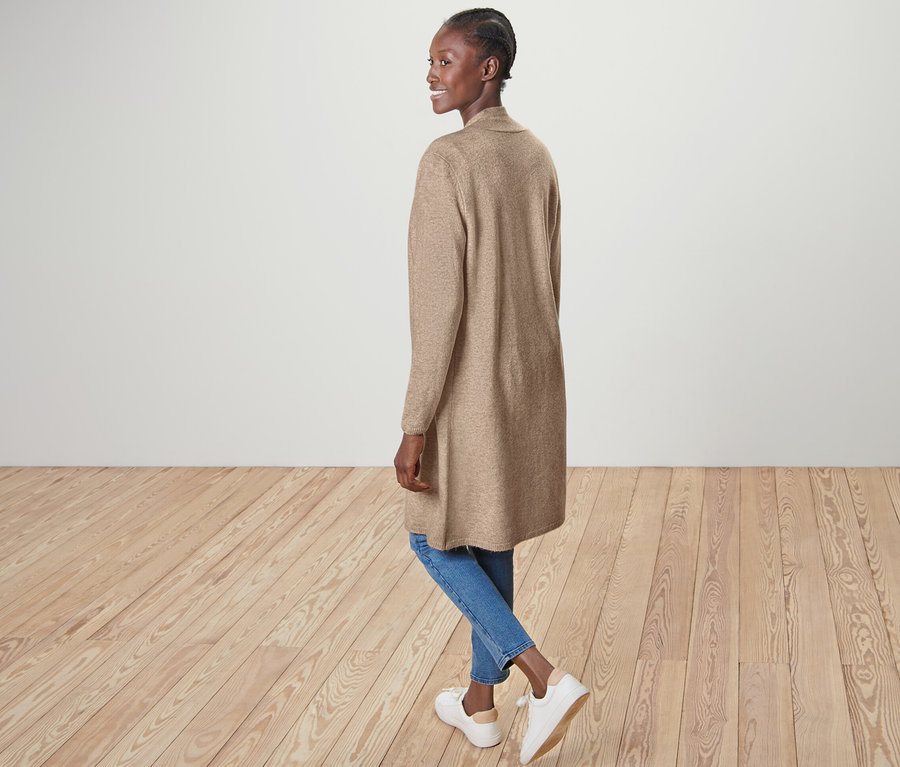 Femme posant en cardigan long ouvert, jean bleu et chaussures blanches.