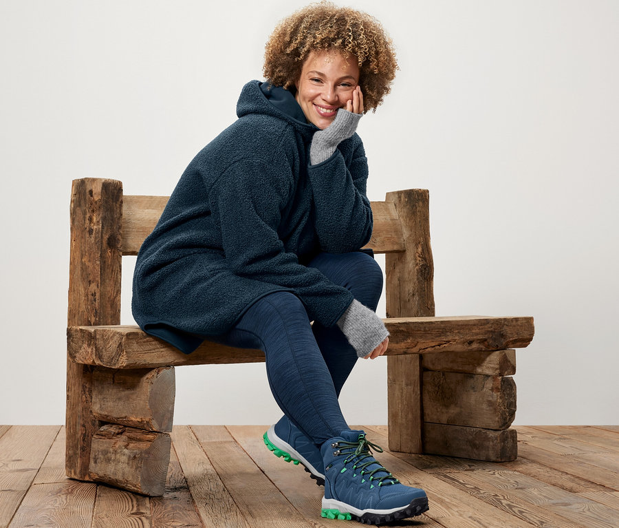 Femme assise sur un banc en bois portant un manteau en teddy oversize et un legging de sport.