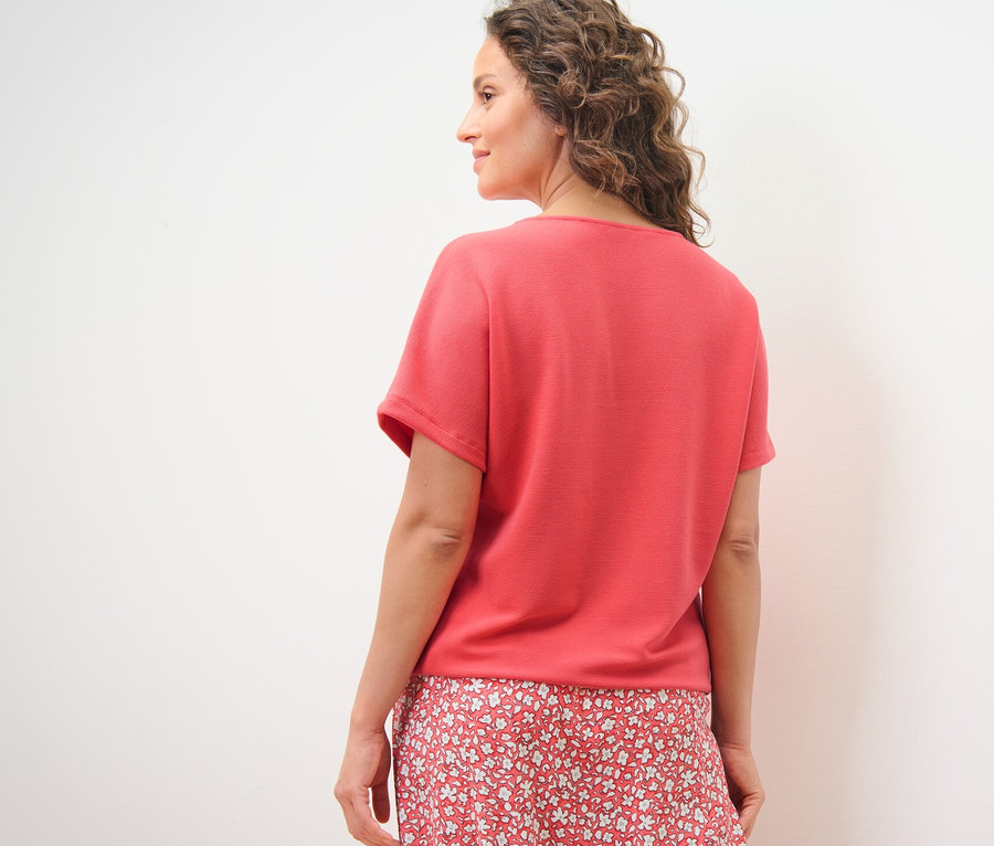 Femme regardant par-dessus son épaule portant une blouse corail.