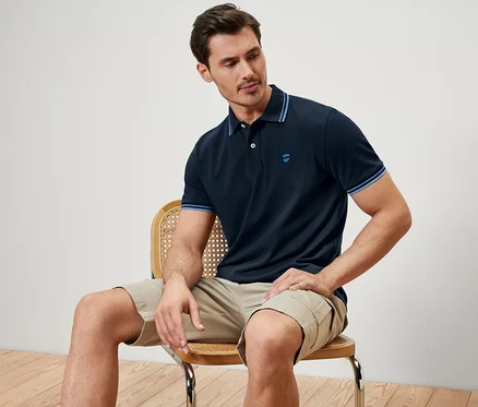 Un homme est assis sur une chaise et porte un polo en piqué bleu foncé.