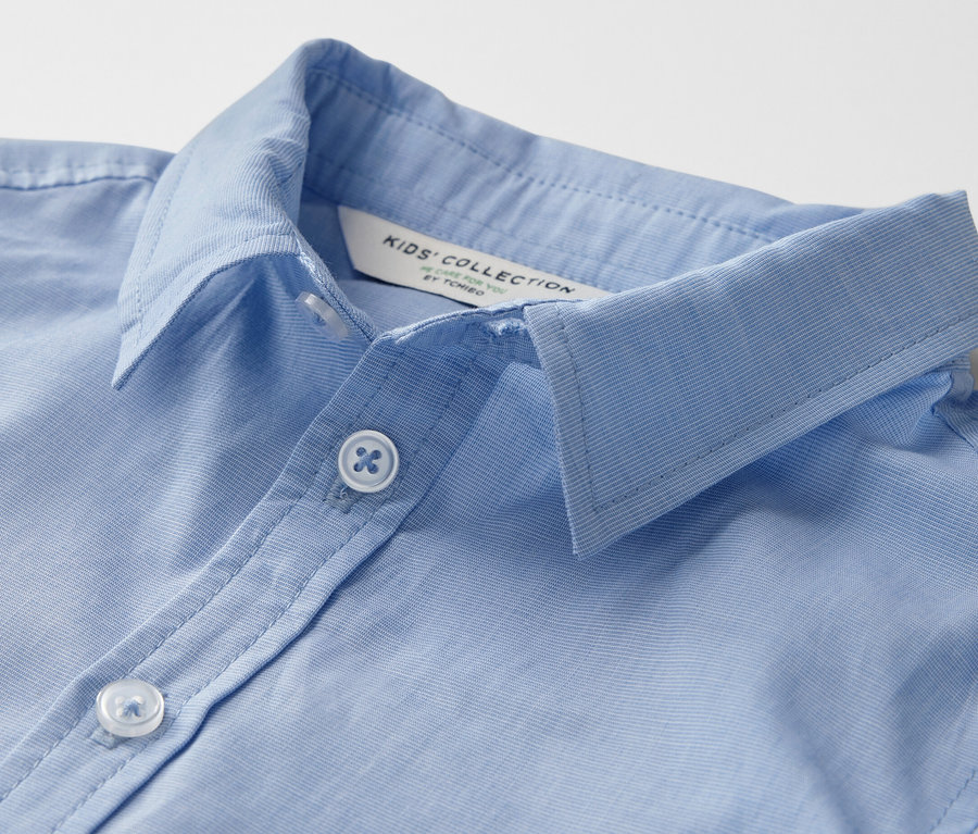 Gros plan d'une chemise pour enfant bleu clair avec col et boutons.