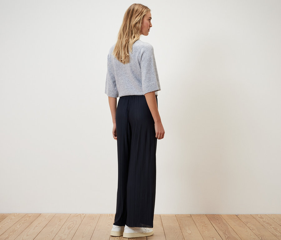 Une femme, vue de dos, porte un pantalon plissé bleu foncé.