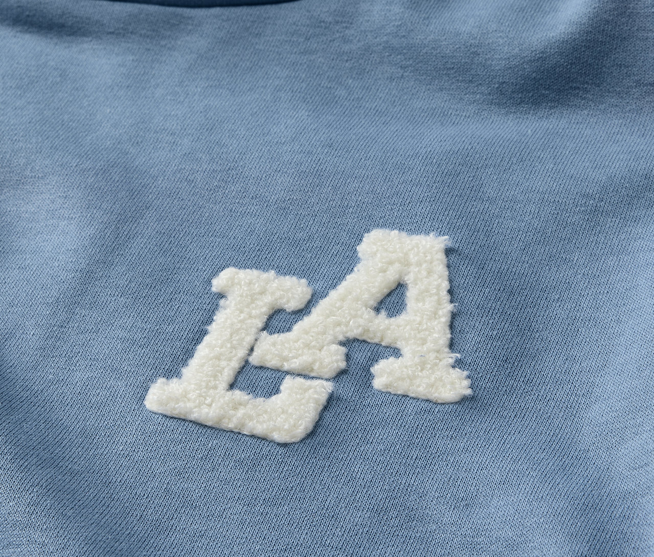 Gros plan sur un sweat-shirt à capuche bleu clair pour enfant avec un lettrage LA blanc.