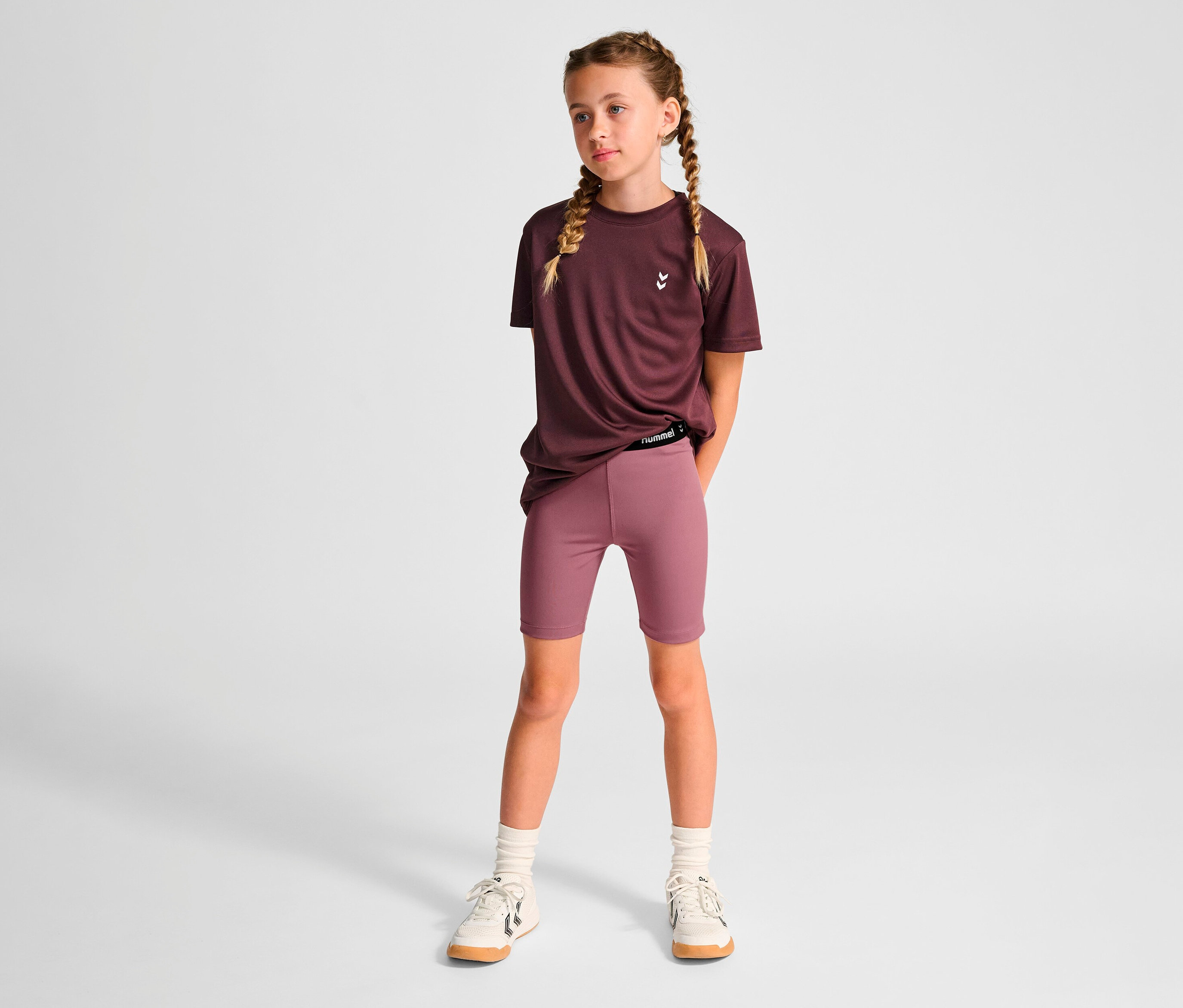 Une fille debout portant un t-shirt violet et un legging court HUMMEL HMLJR Pulse MW.