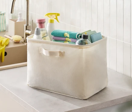 Boîte en tissu beige avec des produits de nettoyage et des chiffons sur un comptoir.