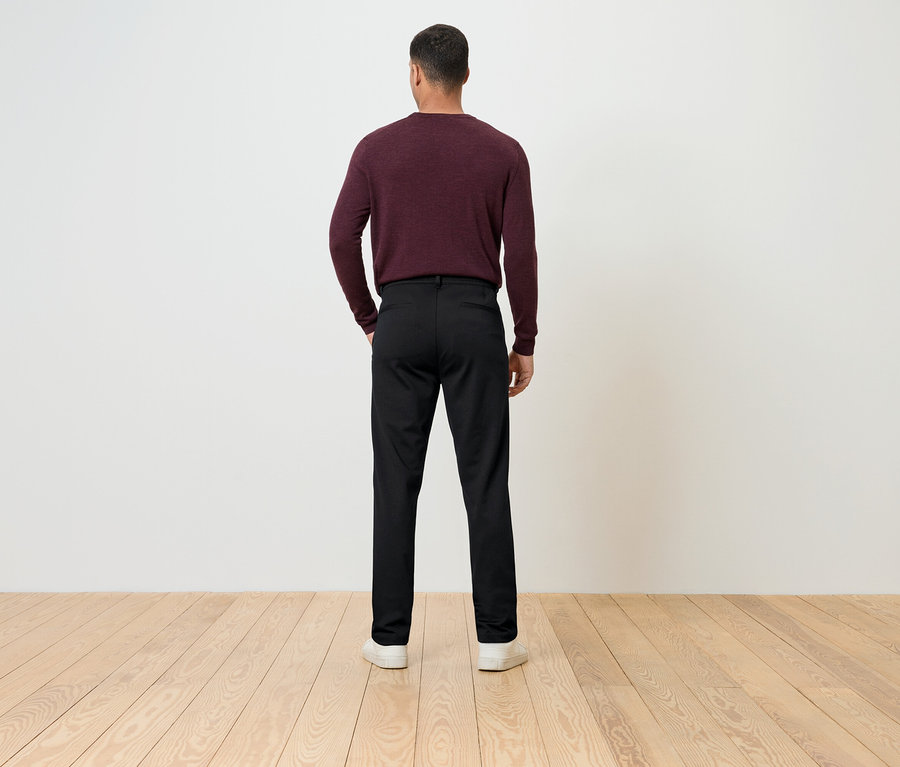 Un homme dos à la caméra porte un pull bordeaux et un pantalon noir.