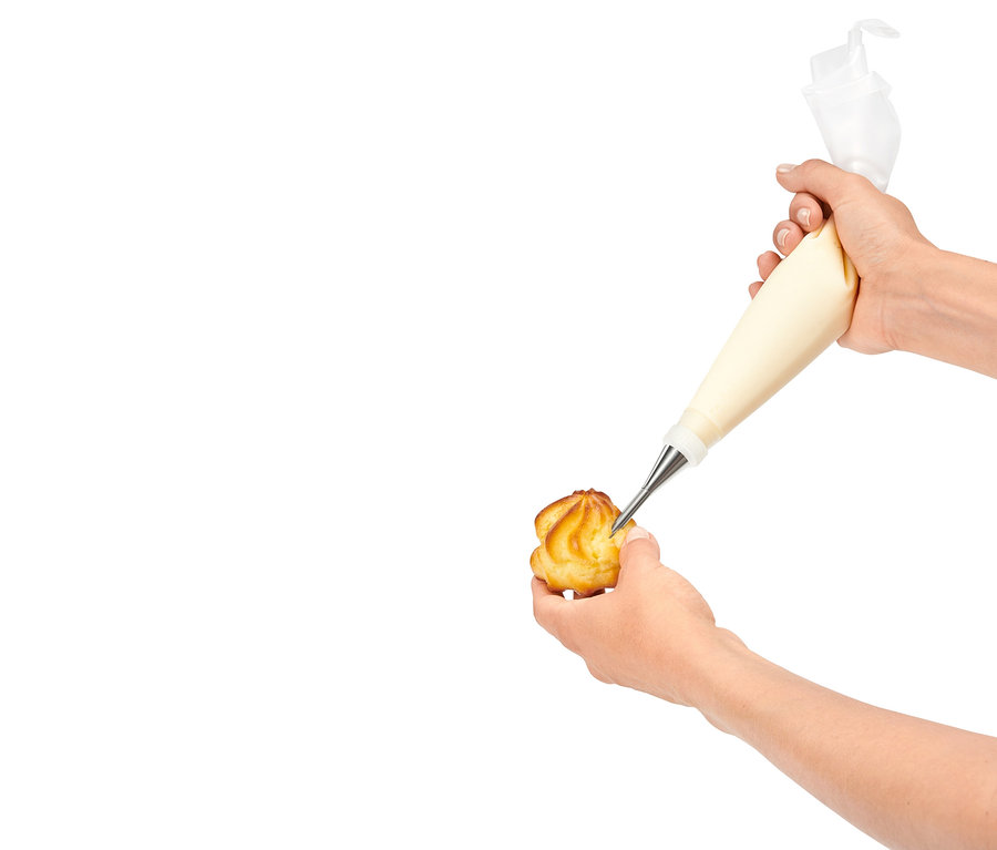 Une main remplissant une pâtisserie de crème à l'aide d'une poche à douille.