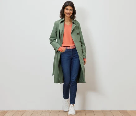 Une femme marche et porte un trench-coat vert clair.