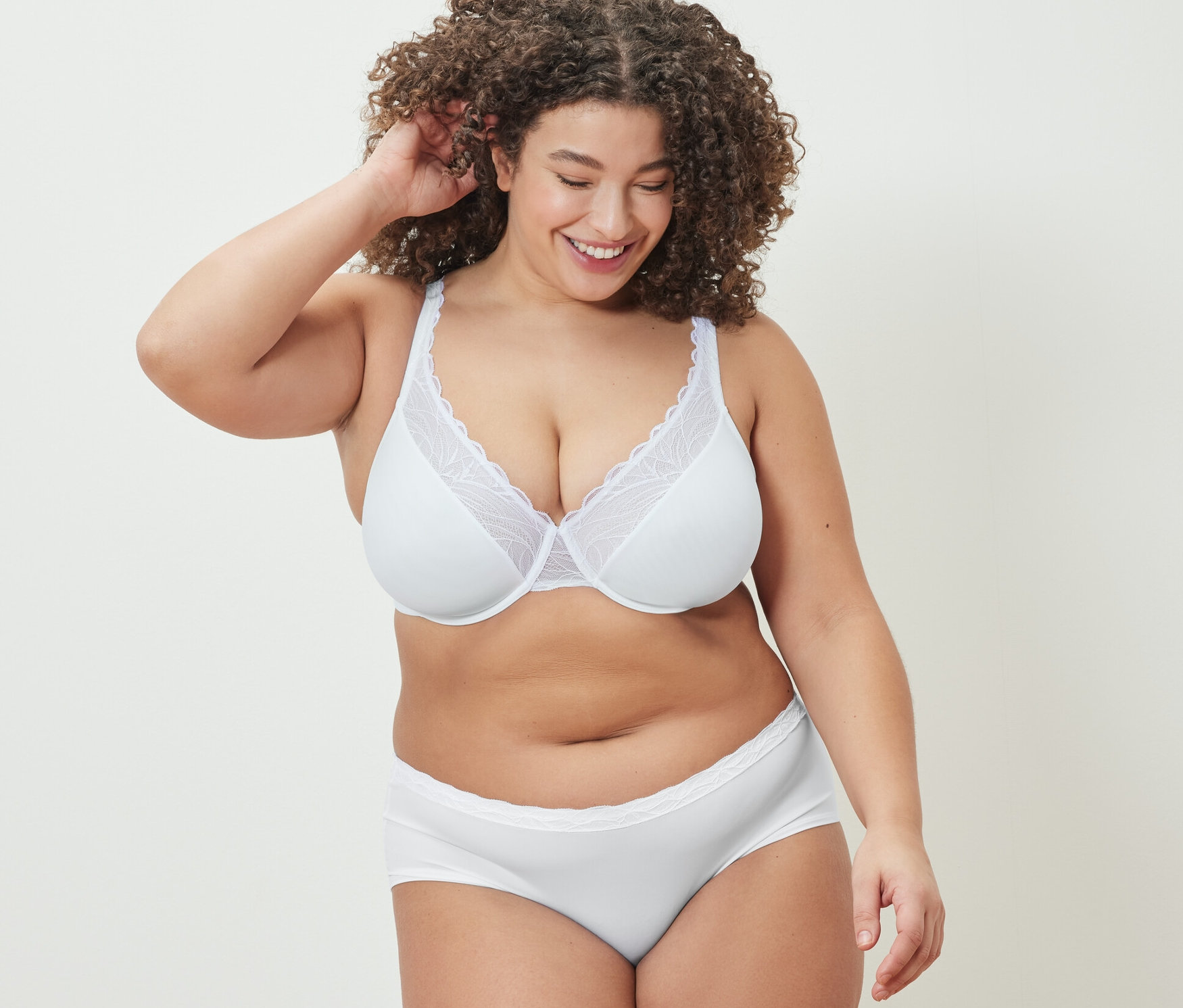 Femme souriante touchant ses cheveux, portant un soutien-gorge à armatures et une culotte blancs.