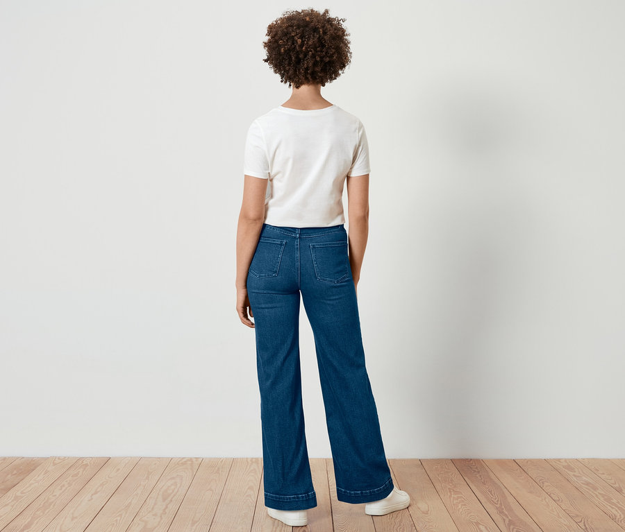 Une femme aux cheveux bouclés se tient dos à la caméra et porte un jean wide leg – coupe « Viki » et un t-shirt blanc.