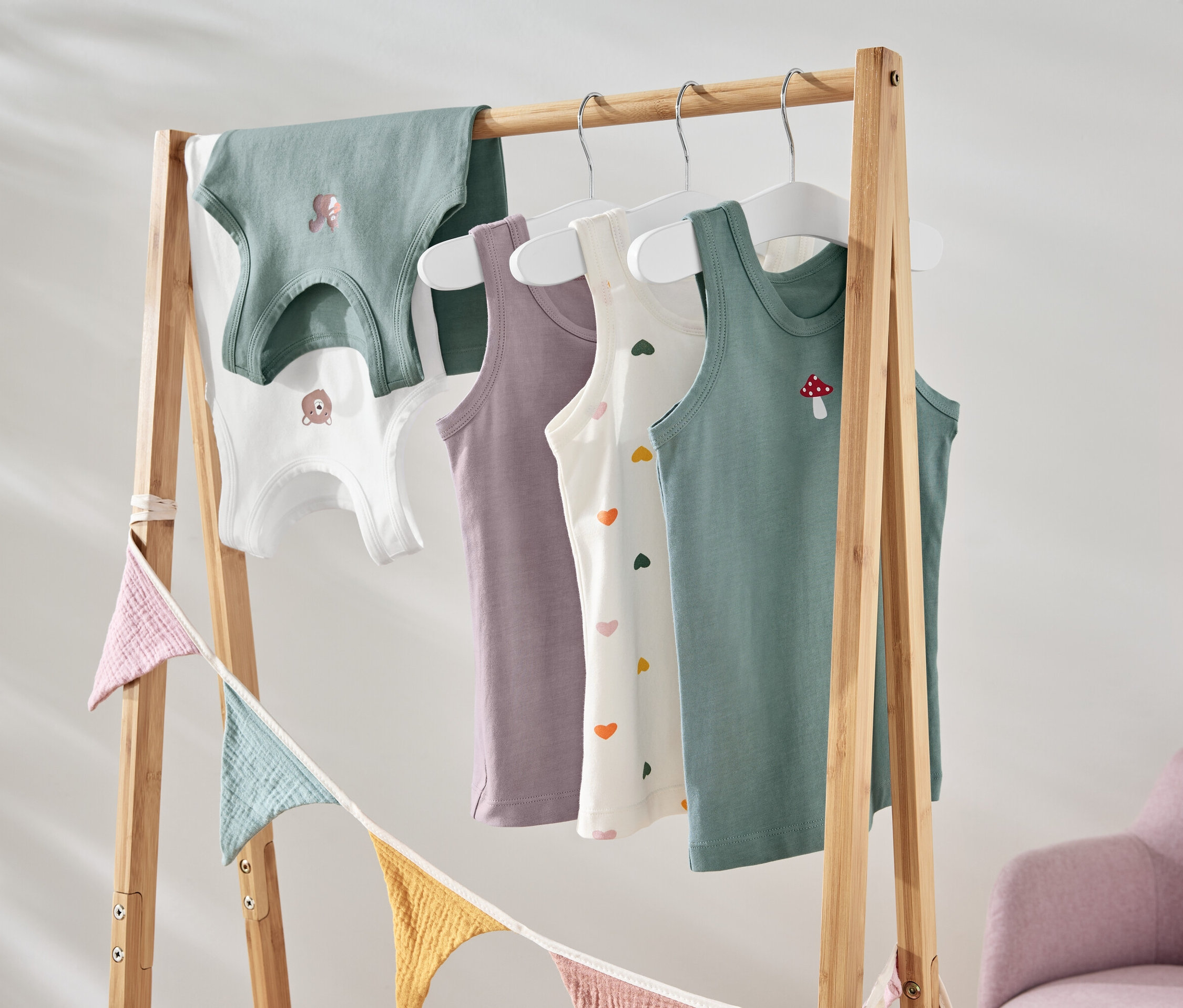 Des débardeurs colorés pour enfants avec différents motifs suspendus à un support en bois.