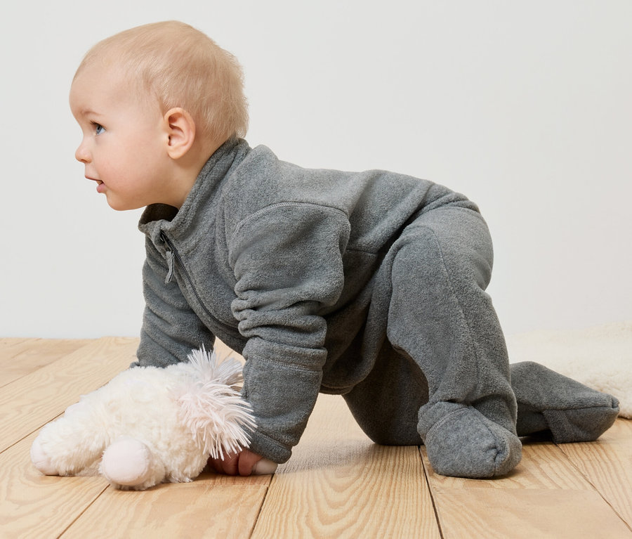 Un bébé en combinaison en polaire rampant sur le ventre à côté d'une peluche.