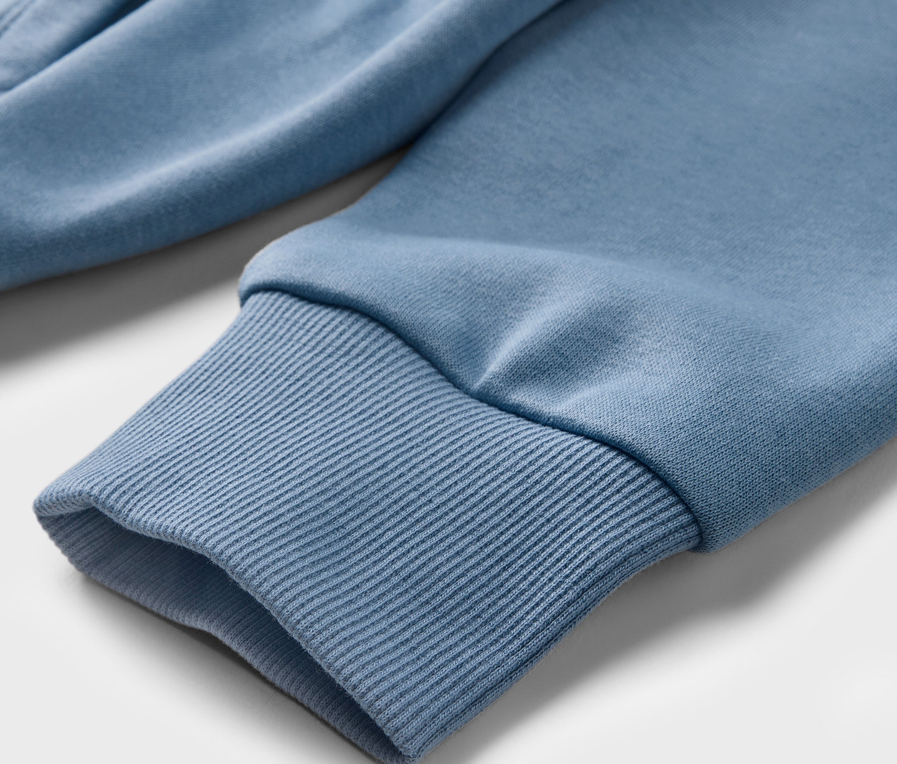 Vue détaillée d'un sweatshirt à capuche bleu clair pour enfant avec un bord côte à la manche.