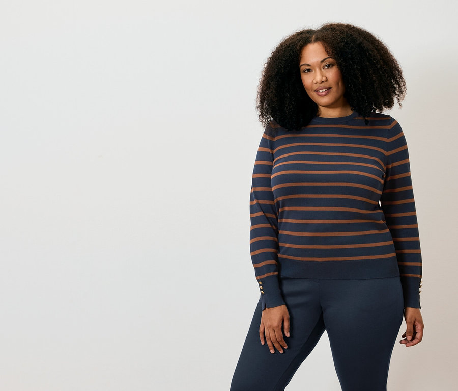 Une femme pose en pull rayé et pantalon.