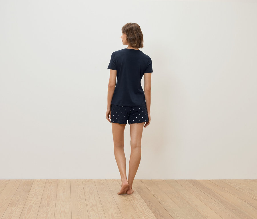 Une femme, vue de dos, porte un t-shirt bleu marine et un short à pois blancs.