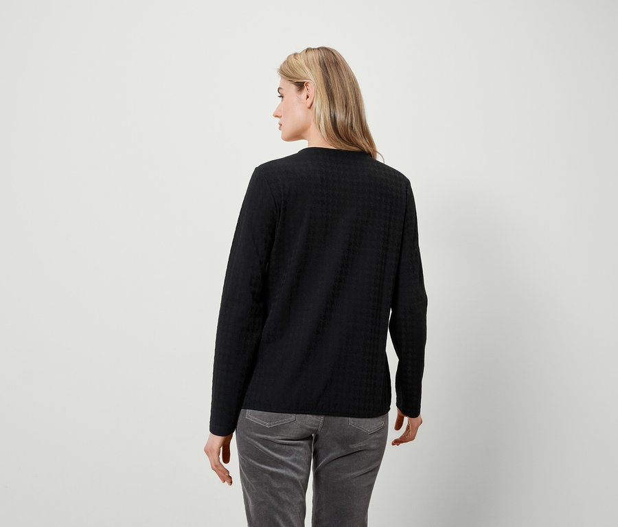 Une femme regarde par-dessus son épaule gauche, portant un t-shirt noir à manches longues et un pantalon gris.