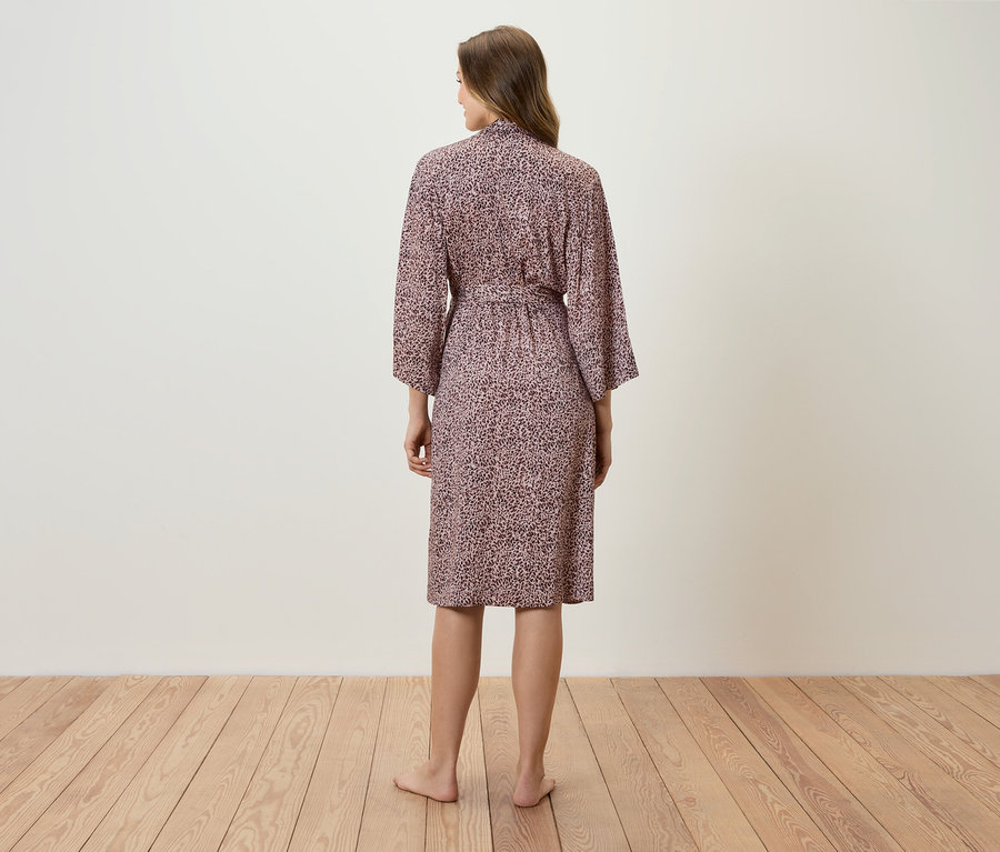 Une femme, vue de dos, porte une robe de chambre rose à motifs.