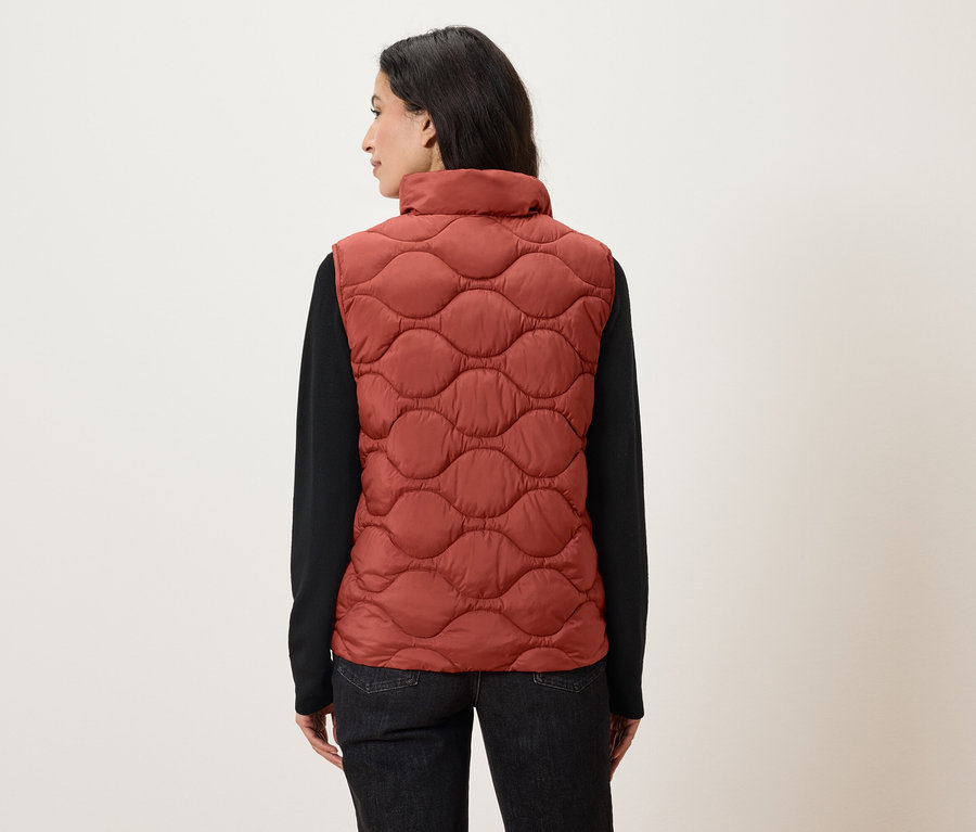 Une femme, dos à la caméra, porte un gilet matelassé orange et une chemise noire à manches longues.