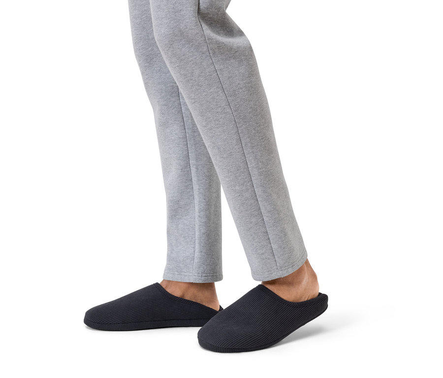 Jambes en pantalon de survêtement gris et chaussons bleu marine sur fond blanc.