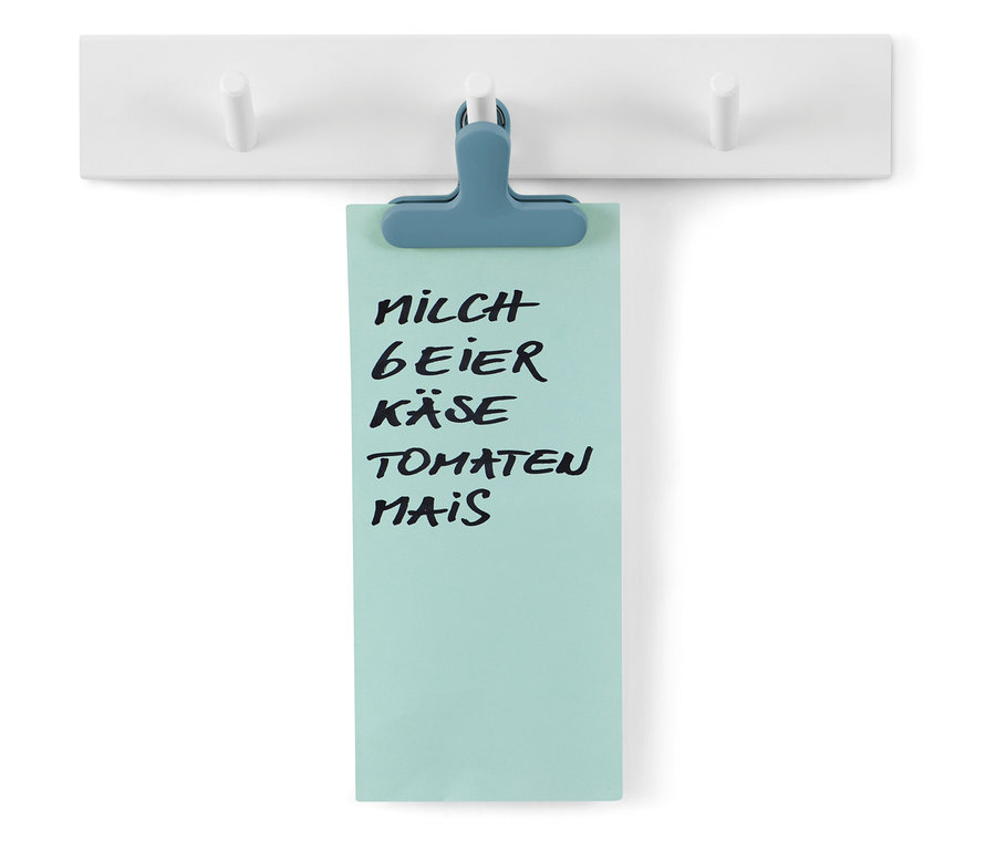 Liste de courses fixée avec un clip bleu sur un porte-manteau blanc.