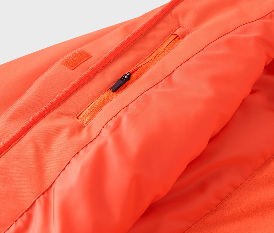 Détail d'une veste orange avec fermeture éclair et poche.