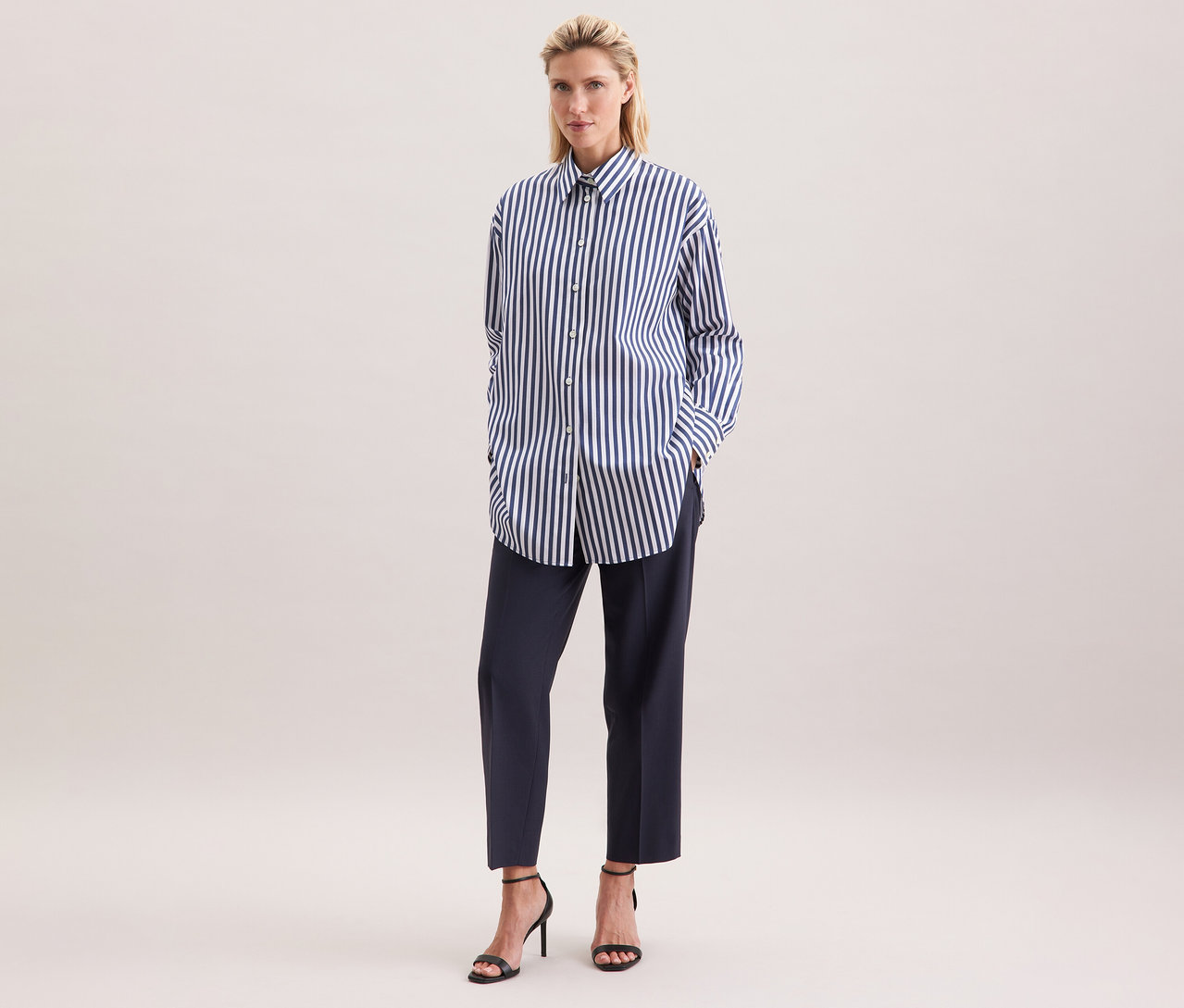 Femme portant une blouse-chemise grande taille Seidensticker à rayures, associée à un pantalon foncé et des talons hauts noirs.
