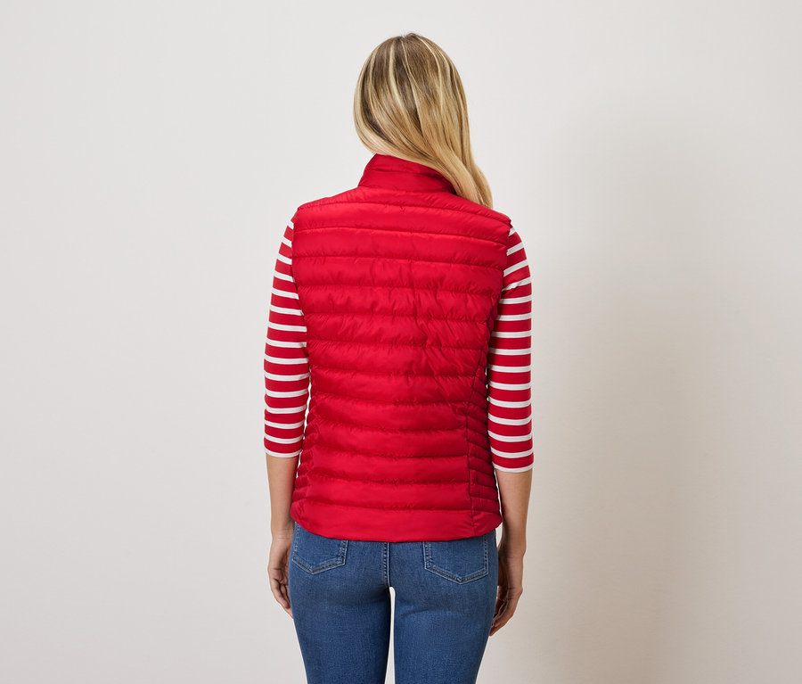Vue arrière d'une femme blonde portant une veste matelassée rouge et un jean bleu.