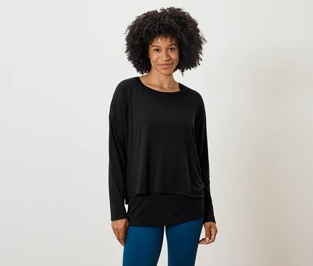 Femme avec une coiffure afro posant dans un haut noir à manches longues et un legging bleu.