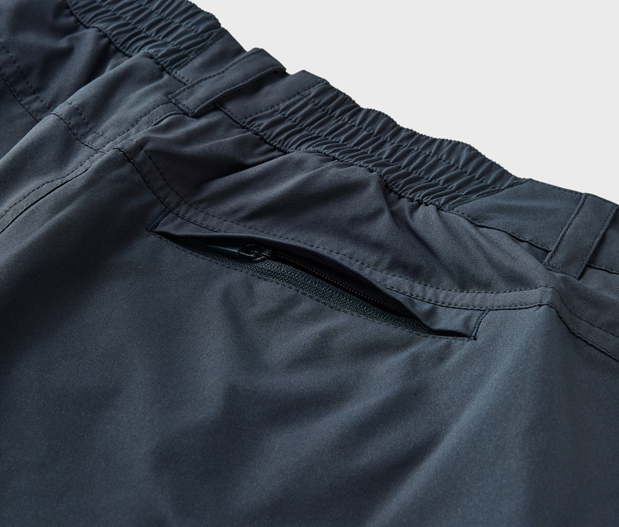 Détail d'un pantalon fonctionnel 2 en 1 bleu avec taille élastique et poche zippée.