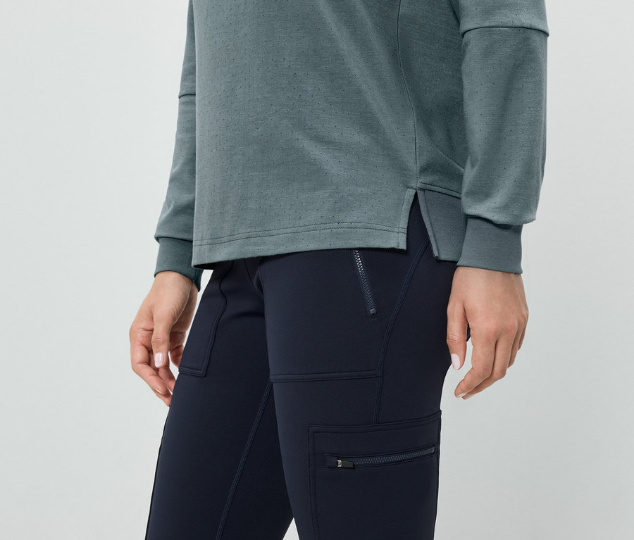 Gros plan d'une femme portant un pantalon bleu marine avec des poches zippées et un haut à manches longues bleu-vert.