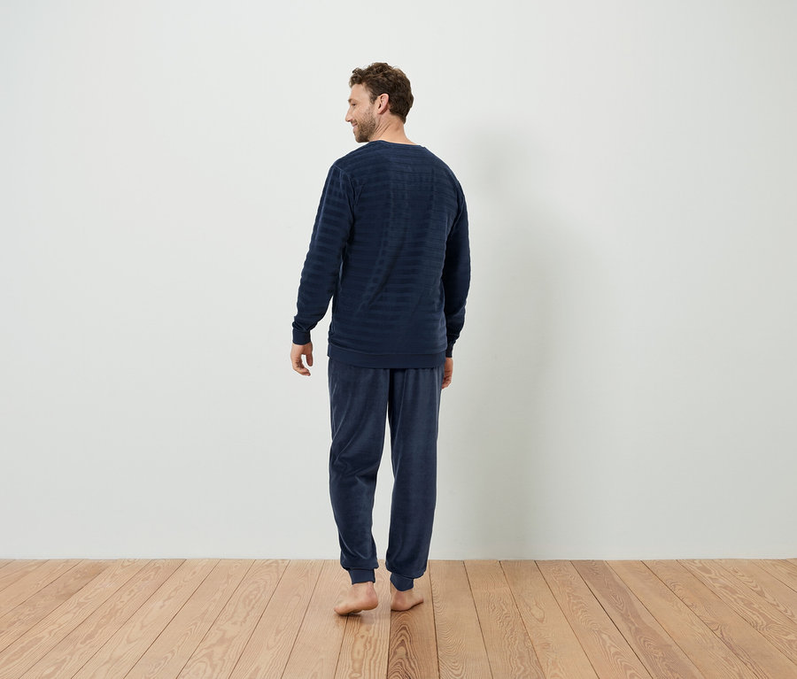 Un homme en pyjama rayé bleu marine, vu de dos, se tient sur un plancher en bois.