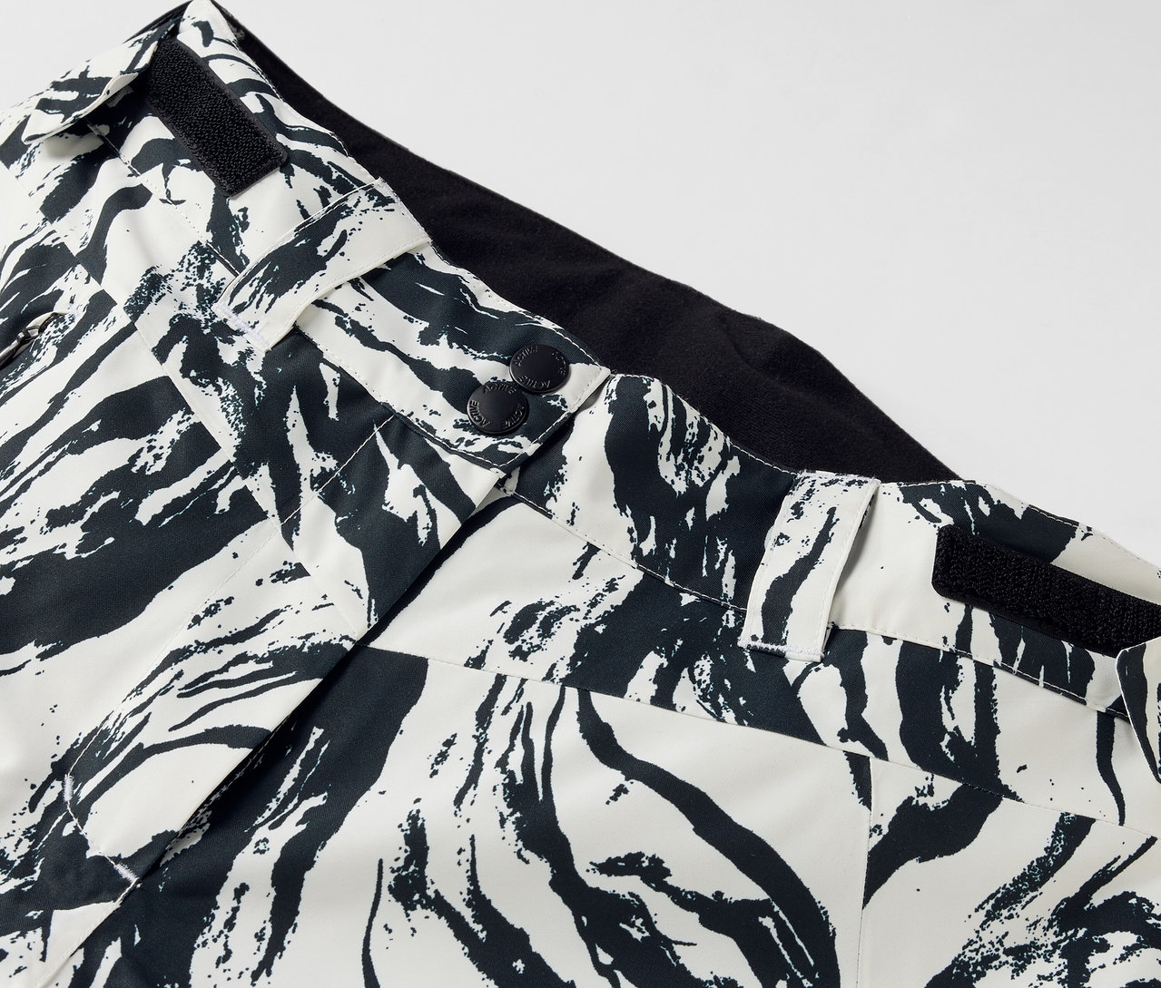 Détail d'un pantalon à motif noir et blanc, fermeture boutonnée et ceinture noire.