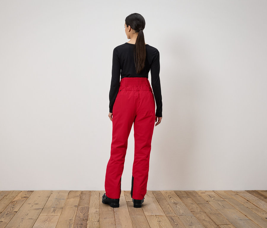 Une femme, vue de dos, porte un pantalon rouge et un t-shirt noir.