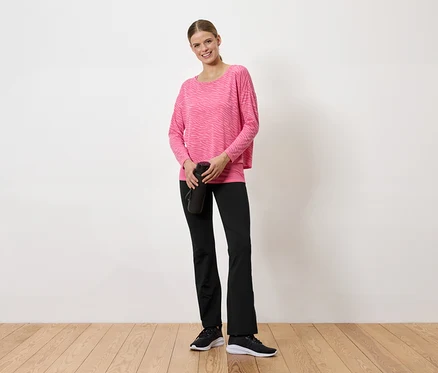 Femme en pull rose et pantalon noir tenant une bouteille d'eau noire.