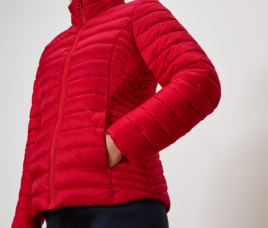 Une personne a une main dans la poche d'une veste matelassée rouge.