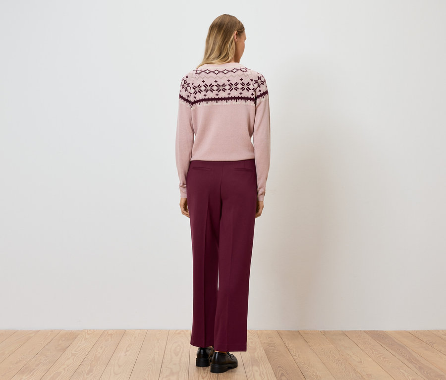 Une femme, vue de dos, porte un pull rose et un pantalon bordeaux.