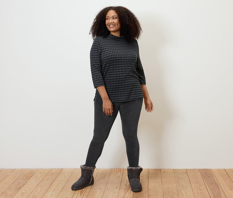 Femme posant en legging en velours côtelé noir, haut à motifs et bottes.