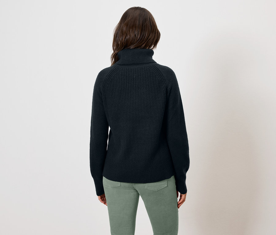 Femme portant un pull à col roulé bleu marine et un pantalon vert, vue de dos.