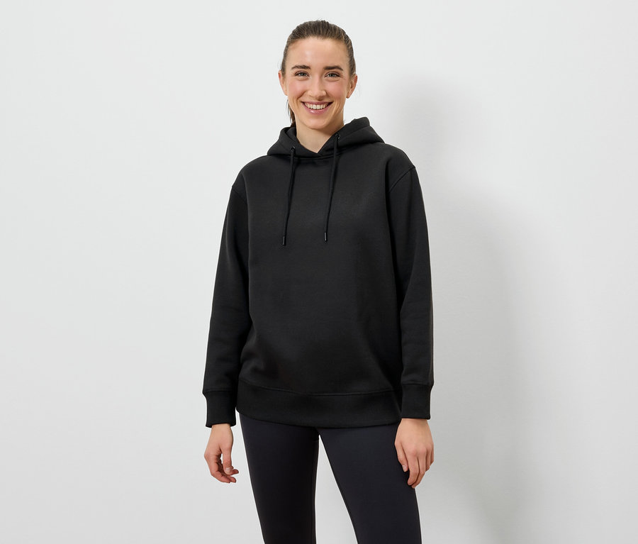 Femme portant un sweat à capuche noir et un legging noir, debout devant un fond blanc.