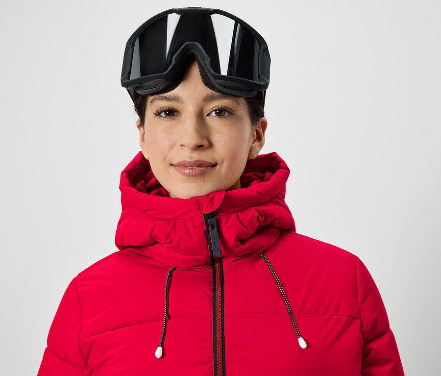 Portrait d'une femme portant des lunettes de ski sur la tête et une veste rouge.