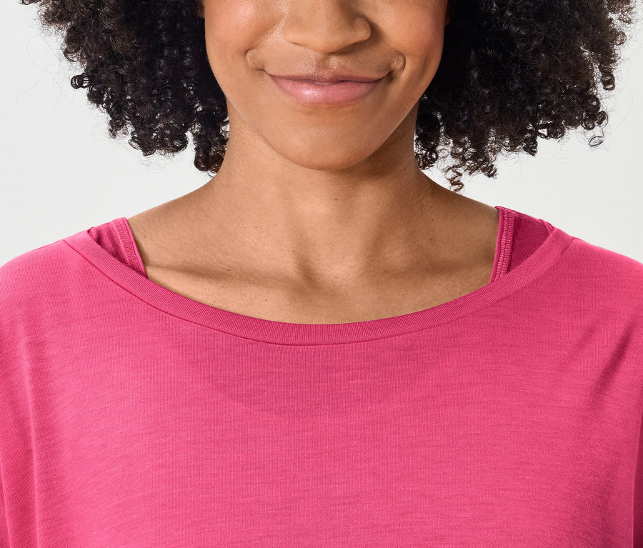 Haut du corps d'une femme souriante aux cheveux bouclés foncés portant un T-shirt rose.