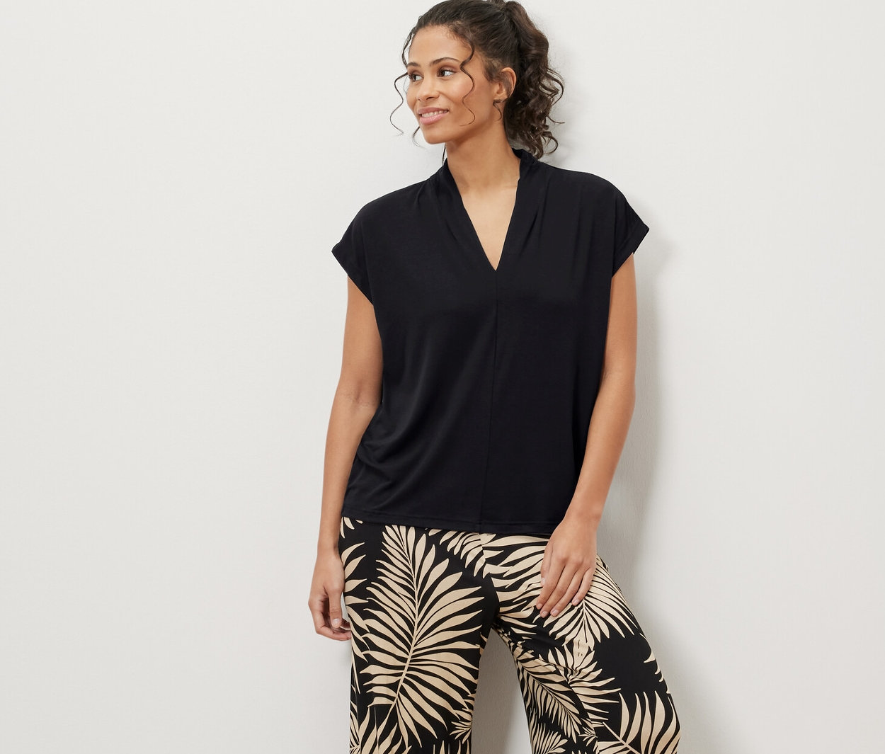 Une femme debout portant une blouse noire avec encolure en V et un pantalon à motif de feuilles.
